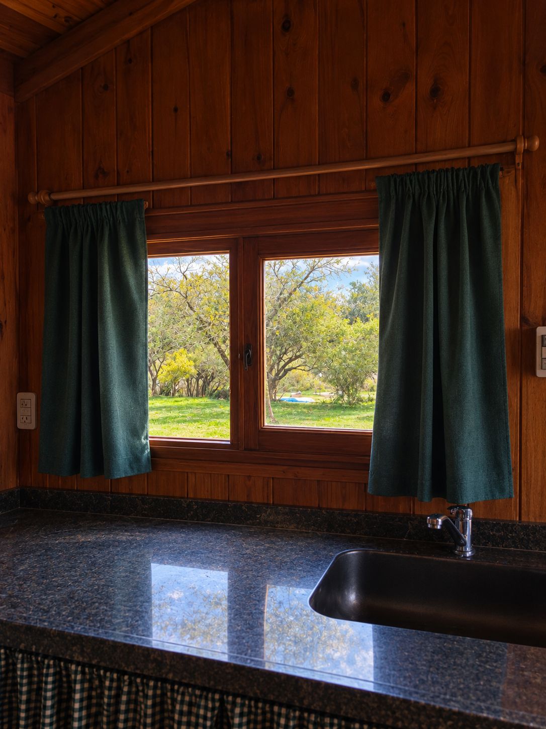 Mesada de granito con bacha, frente a una ventana con cortinas que da al parque