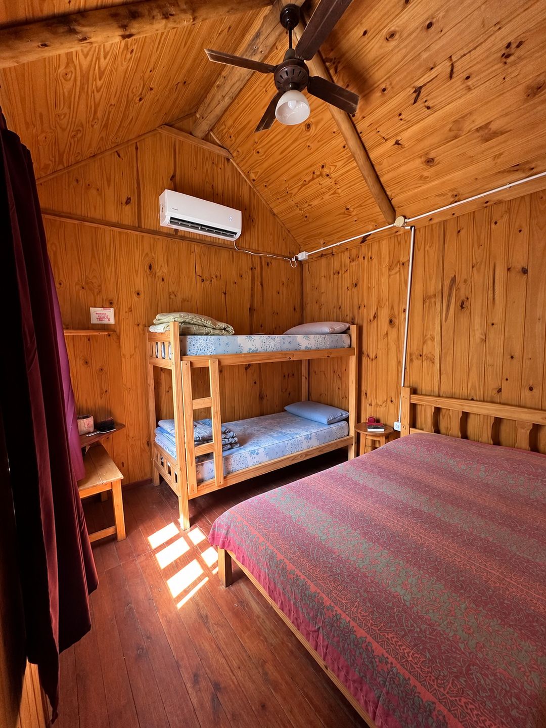 Interior de la cabaña: cama matrimonial y cucheta de madera, ventilador de techo y aire acondicionado