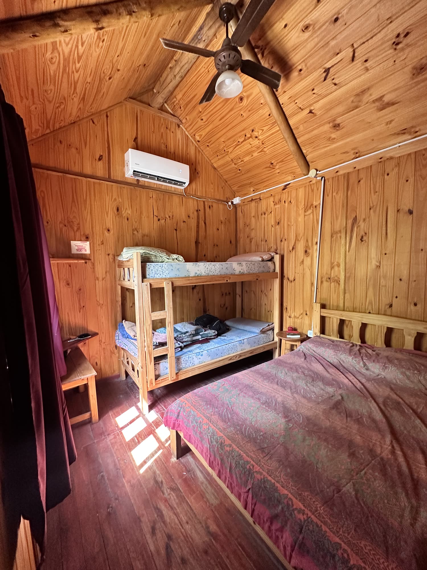Interior de la cabaña: cama matrimonial y cucheta en madera, con aire acondicionado y ventilador de techo