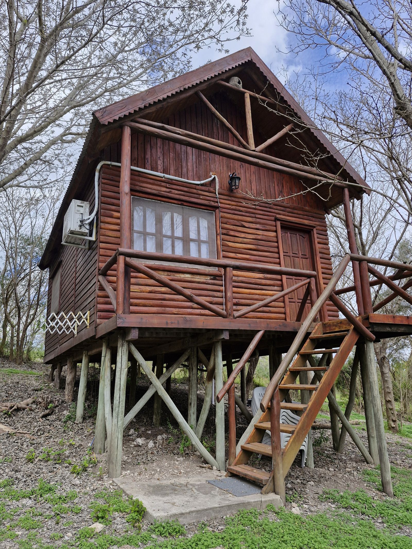 Cabaña de madera de dos plantas sobre pilotes, con escalera y balcón
