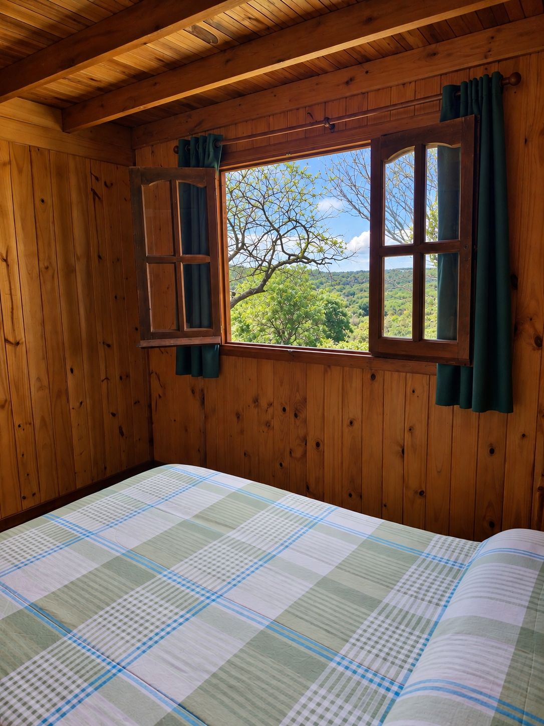 Cama matrimonial junto a una ventana abierta con vista a los árboles