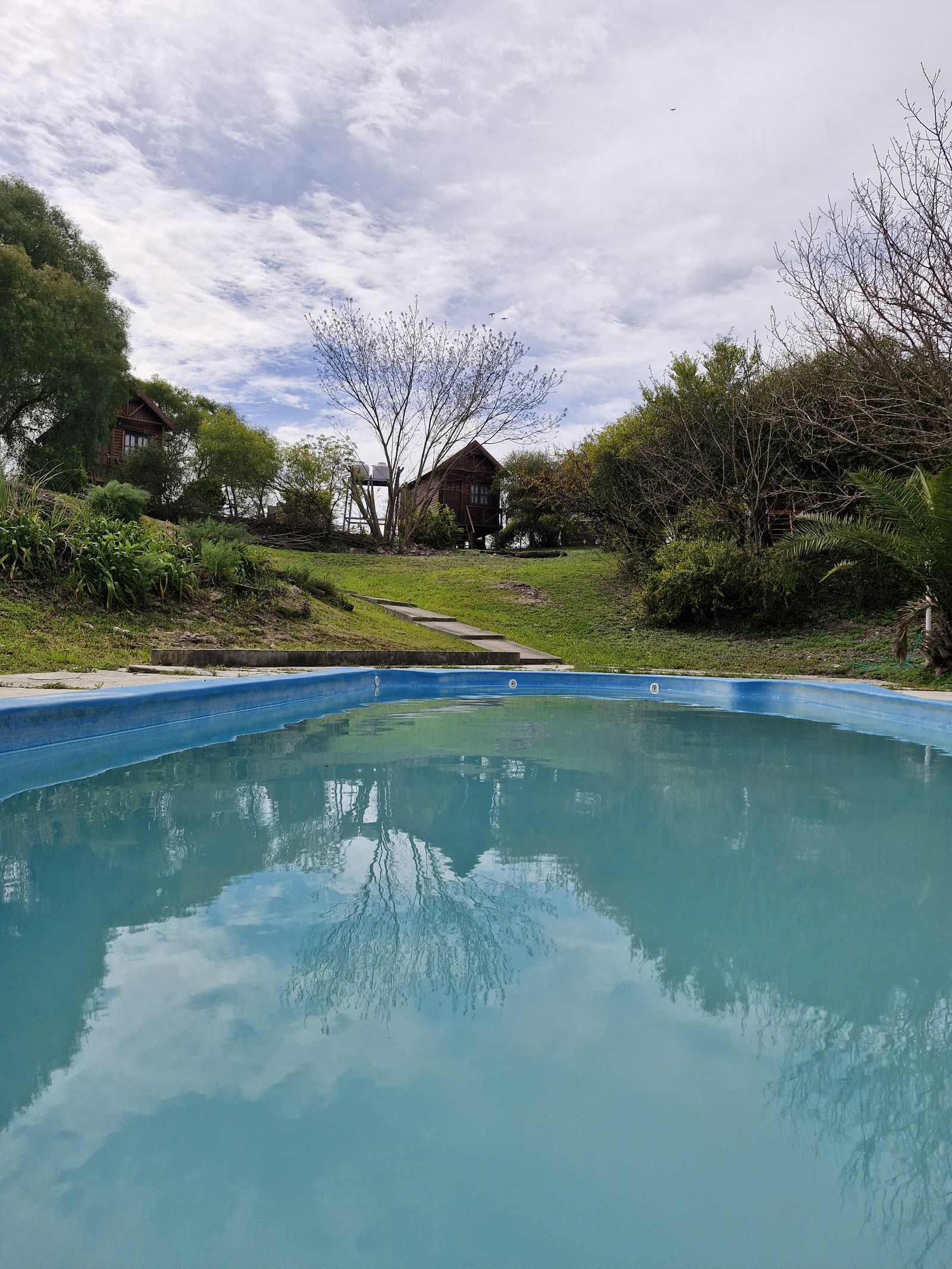Piscina con el reflejo del cielo; detrás, el parque y las cabañas