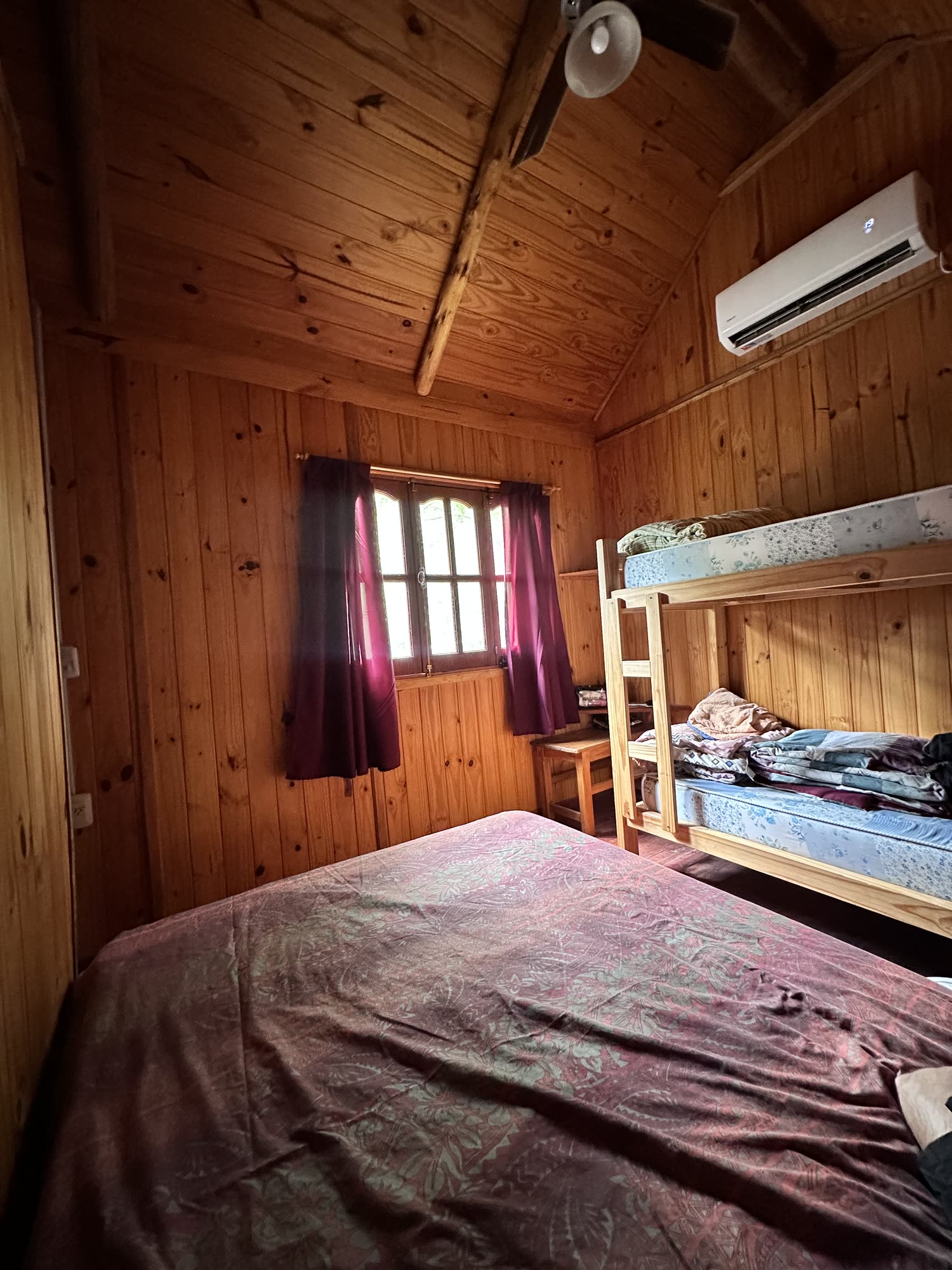 Dormitorio de la cabaña con ventana y cortinas, todo revestido en madera